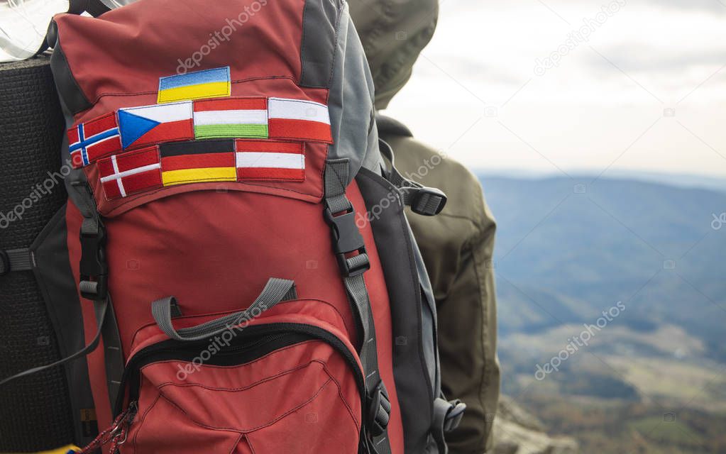 travel and hiking life style photography concept picture of different European countries flag stripes on backpack in mountains route environment with blurred background copy space for your text here 