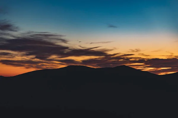 beautiful natural wallpaper background landscape photography of dramatic orange and blue sunset cloudy sky and dark mountain ridge silhouette, empty copy space for your text here