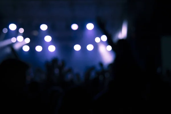 unfocused blurred night club party scene of people silhouettes on music stage blue bokeh illumination background in performance time