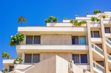 Ucuz otelin dış cephesi, teraslarda yeşil ağaçlar ve açık hava saatinde balkon.  