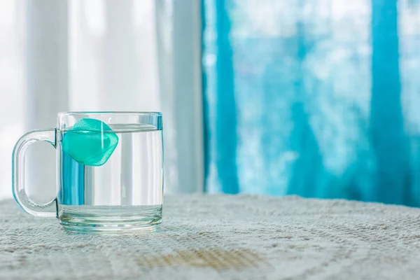 water with ice in cup on table white interior and blue curtains unfocused background, warm summer season concept photography, empty copy space for your text