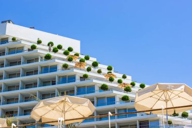 Beyaz otelin dış cephesi terasları yeşil çalılar ve şemsiyelerle açık havada ön planda güzel yaz tatilleri için güzel bir yer, metin için boş kopya alanı 