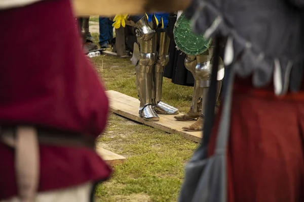 reconstruction middle ages festival and stainless steel knight armor boots center of composition in textile red cloth unfocused foreground frame