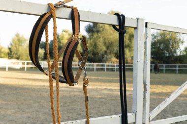 Çiftliğin metalik çitlerinde asılı duran ata binmek için tasma ve kemer ekipmanları. 