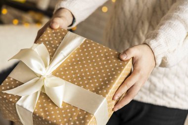 İnsan eliyle fiyonklu Noel hediyesi karton kutusu. Konsept fotoğrafçılık. İç mekan, odaklanmamış çelenk aydınlatma. 