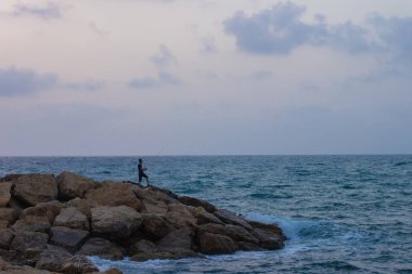 Balıkçılık yaşam tarzı hobi. Kayalık deniz kıyısı manzarasında siluet. Alacakaranlık fırtınalı hava zamanı. 