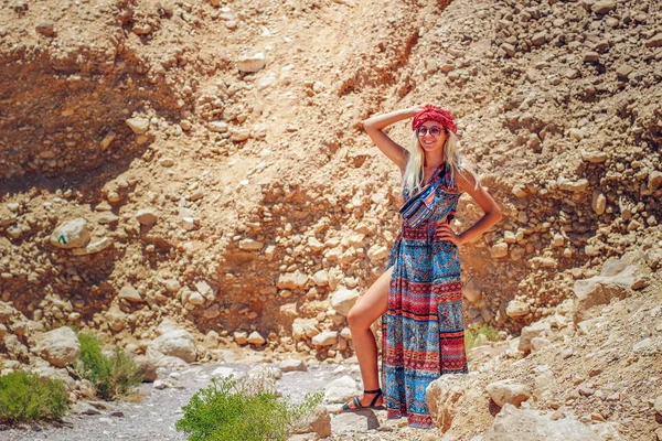美しいフォトジェニックな笑顔のファッション写真カラフルな長いドレスでセクシーなウクライナ人女性イスラエルの砂漠の峡谷の荒野と危険な自然環境の石の上に足でポーズ — ストック写真