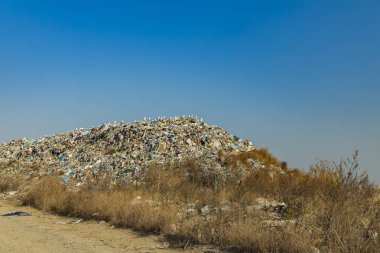 Küresel çevre kirliliği konsepti: Kenar mahallelerdeki çöplük tepesi, kırsal alandaki mavi gökyüzü arka planı, metin alanınız için boş kopya alanı 