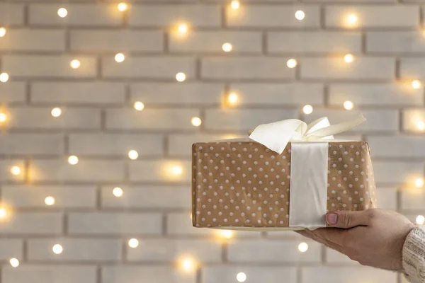 Christmas gift in hand box with bow brick wall garland illumination unfocused bokeh background wallpaper pattern concept picture with empty copy space for your text here