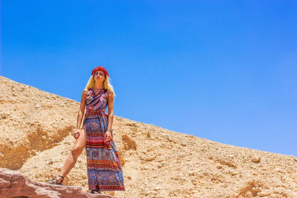 白いヨーロッパの女性穏やかな肖像画でHihabとカラフルなロングドレスで支配的なポーズでカメラを見て上から砂漠の峡谷の岩の環境で崖の上に滞在 ファッションポスター コピースペース — ストック写真