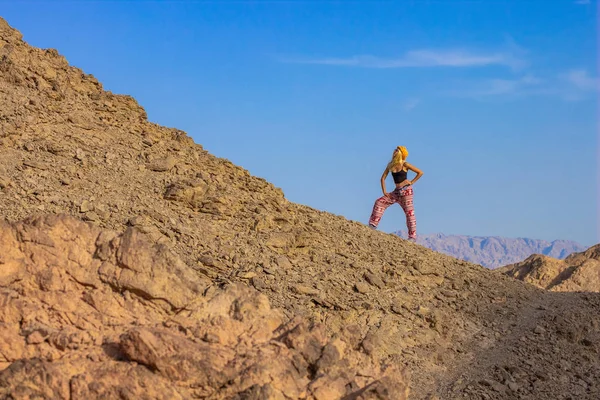 travel photography concept funny woman pose in happy mood on desert sand stone rocky mountain scenic landscape environment on empty blue sky background , copy space