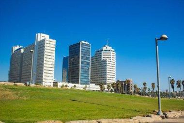 Yaz zamanı Tel Aviv İsrail 'in başkenti kent simgesi yeşil çimen kare sokak feneri önplanı ve gökdelen binaları açık mavi gökyüzü arkaplanı 
