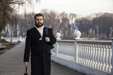 Orta yaşlı, sakallı bir adam soğuk bir sabah parkında arka planda mermer çitlerle işe gider. 