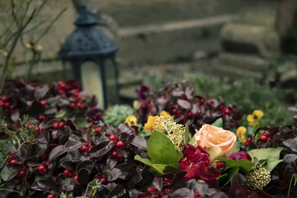 Cemetery grave flower bed with flowers sadness mood concept and gothic atmosphere with blurred background of handle lantern — Stock Photo, Image