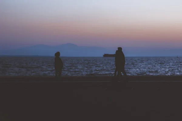 Lidé silueta promenáda ve večerních hodinách na nábřeží okresu s tmavým mořem horizont pozadí s prázdným kopírovacím prostorem pro váš text zde — Stock fotografie