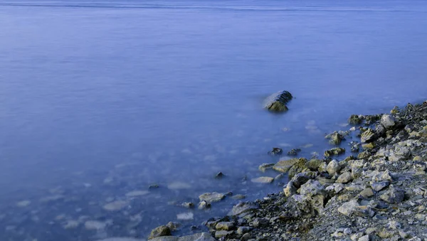 Línea de costa de piedra frente al mar paisaje de fondo exposición larga superficie del agua crepúsculo tiempo espacio de copia vacío — Foto de Stock