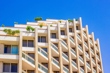 Beyaz kirli duvarlı otel dış cephesi teraslarda pencere ve ağaçlar, yaz tatili sezonu mavi gökyüzü arka planı