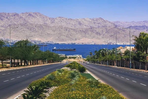 Eilat Israeli city nature scenic landscape photography of car road way down to Gulf of Aqaba Red sea bay shoreline district with view on a water port area cargo ship and mountains background — Stock Photo, Image