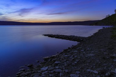 sakin uzun pozlama manzara huzurlu göl suları taş kıyı şeridi güneş doğmadan önce insanlar olmadan alacakaranlık ışığı altında