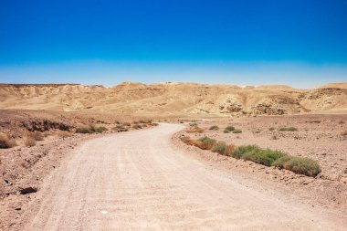 Çöl manzarası, kum vadisi, toprak yol önü ve kayalık dağ sıraları arka planda yaz mevsimi, sıcak İsrail kırsal bölgesi manzarası, kopyalama alanı.