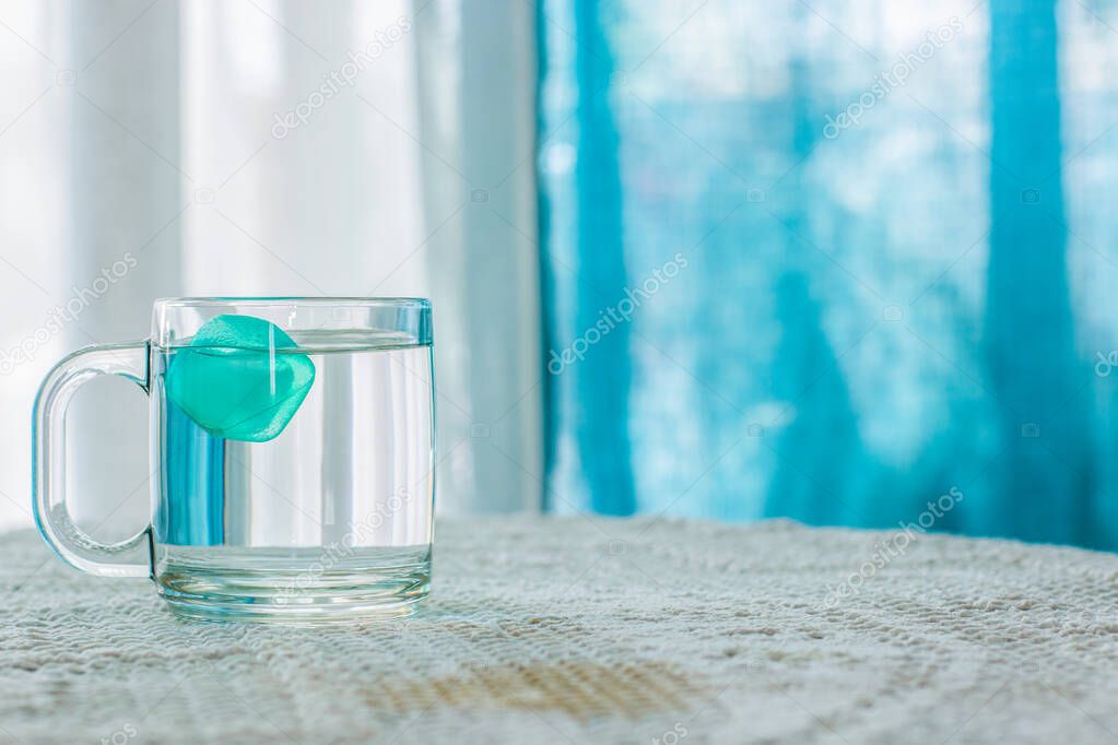 water with ice in cup on table white interior and blue curtains unfocused background, warm summer season concept photography, empty copy space for your text