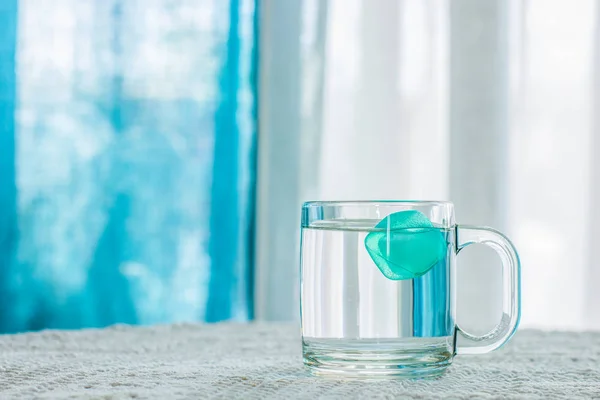 health care life style concept picture of cup of water with peaceful of ice inside in summer hot weather time on indoor room table interior environment white and blue curtain background, copy space