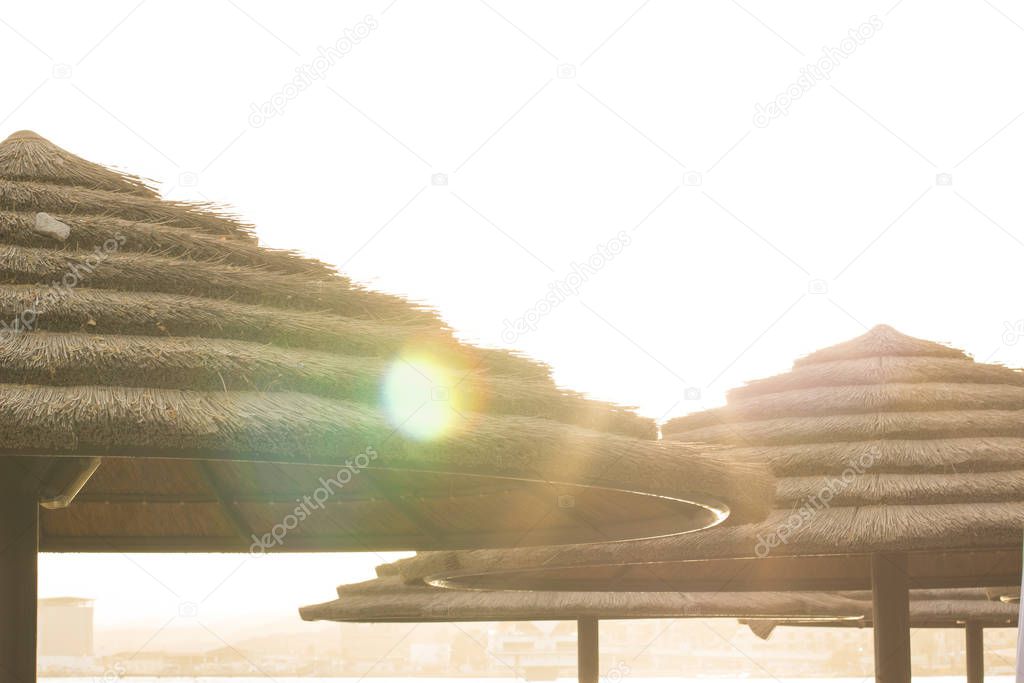 abstract unfocused summer vacation on a beach concept bright picture of straw umbrella silhouettes in sun light glares on white sky background, empty copy space for text