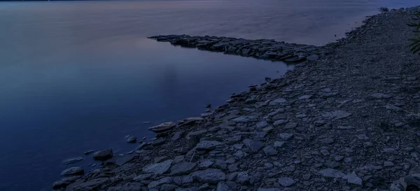 Длительное воздействие пейзаж полночь синий тонизирующий стиль фотографии мирной водной береговой линии живописный вид каменистый грунт и природный пирс мирный открытый фон окружающей среды с пустым копировальным местом — стоковое фото