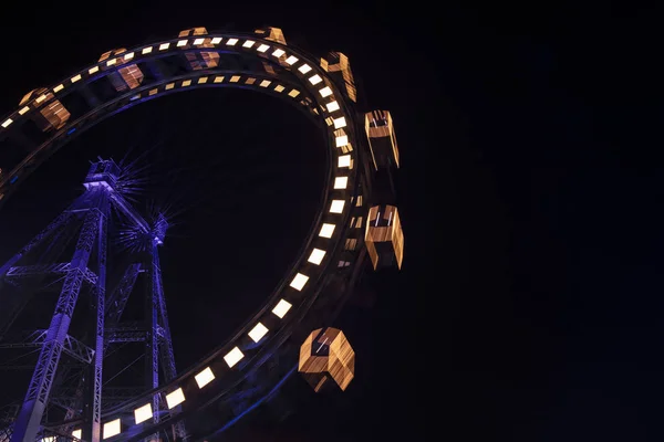 Carnival entertainment Ferris wheel motion with dark blue illumination from frame and yellow from cabins at night time black sky background empty copy space for your text here