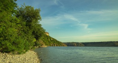 summer time landscape scenic view hill land coast line of lake peaceful waters near forest edge green foliage nature reserve environment blue sky background empty copy space for text