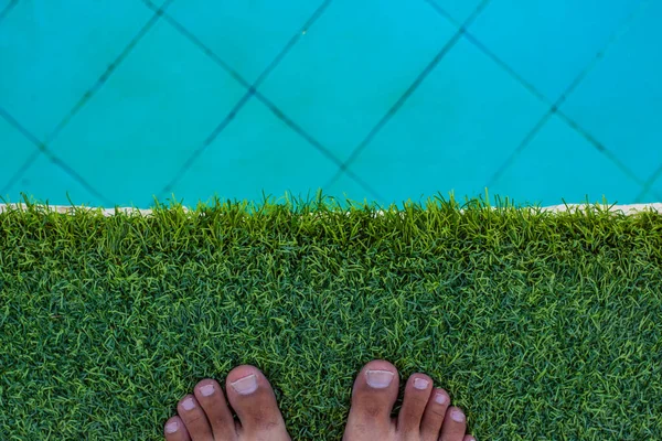 夏休みシーズンスイミングプールホテルリラクゼーションスペース背景に男性の裸の足で合成芝の床,空のコピースペースあなたのテキストはこちら — ストック写真