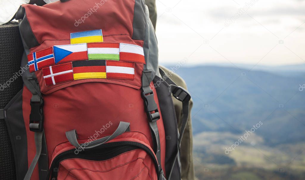 travel life style passion concept picture of backpack with country flags stripes of Ukraine, Germany, Austria, Denmark, Norway, Hungary and Czech Republic blurred background mountains highland view