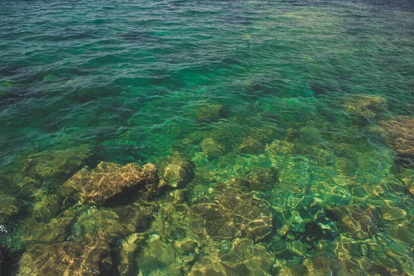 Spiaggia rocciosa Mar Egeo lungomare con onde prima della tempesta in tempo ventoso e luminoso colorato periodo di vacanza estiva, nebbioso sfondo silhouette di montagna — Foto Stock
