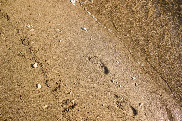 Spokojna piaszczysta plaża z ludzkimi stopniami odcisków stóp na nabrzeżu wzdłuż lekko falującej niebieskiej linii brzegowej wody — Zdjęcie stockowe