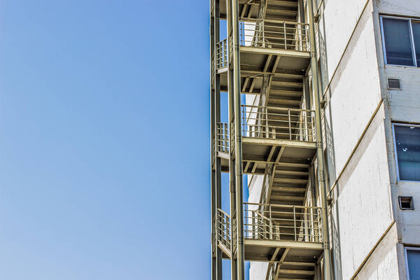 Metal fire escape stairs construction outdoor side of high building and empty blue sky, copy space for text