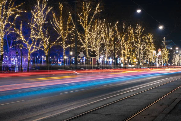 Μεγάλη έκθεση νύχτα φως της πόλης εορταστική δρόμο αστική άποψη πολύχρωμο φωτισμό από χνουδωτά αυτοκίνητα προβολείς και γιρλάντες στα δέντρα — Φωτογραφία Αρχείου