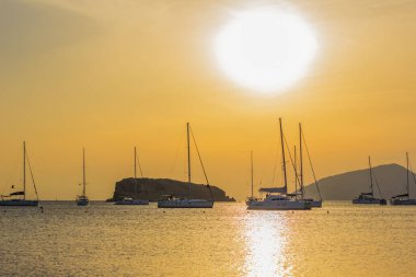 Pahalı görkemli lüks Akdeniz körfezi kıyı şeridi manzaralı kayalık uçurumlar su ve yat siluetleri üzerinde canlı turuncu günbatımı aydınlık gökyüzü arka planı