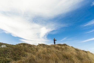 Kameraya geri dönen adam tepenin üstünde rüzgarlı bir paltoyla poz veriyor başarılı bir yaşam tarzı konsepti fotoğrafçılığı dağ doğası dışında mavi gökyüzü arkaplan alanı kopya veya metin için
