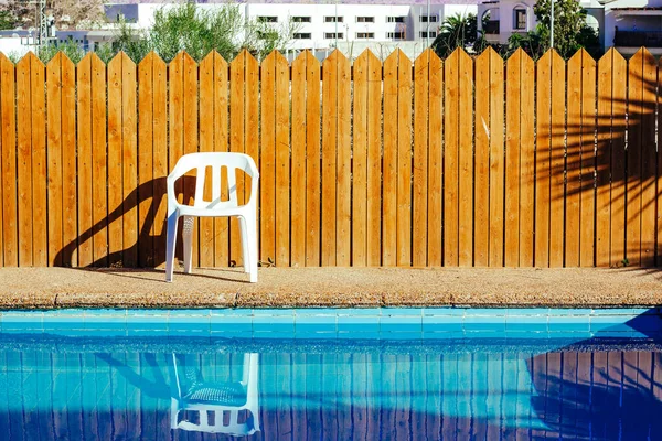 pool side suburban villa back yard space without people here white plastic chair and wooden wall background with lights and shadows in summer sunny day time copy space