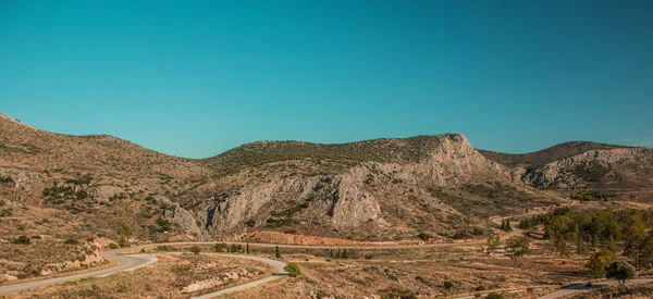 Vahşi Batı Amerika Birleşik Devletleri panoramik manzara manzarası vahşi doğa manzarası kayalık tepeler kırsal alan kavisli yalnız araba yolu ve açık mavi gökyüzü arkaplanı, metin için boşluk kopyalama