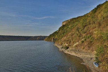 Ulusal park manzarası huzurlu göl manzarası yalnız kırsal kayıkla kıyı şeridi ve yeşil kayalık tepe arazi mavi gökyüzü arkaplan alanı ile gündüz vakti