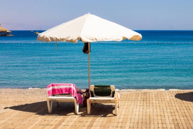 Otel tatil beldesi sahil güvertesi sandalyesi ve şemsiye mobilyaları yaz tatili tatil sezonu konsepti olarak Kızıldeniz rıhtımında insanlar olmadan hareket ettiriyor.