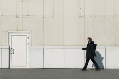 Maske profili fotoğrafçılığı yapan tek bir adam kendini izole etme ve sosyal uzaklık şehir çevresi kavramı kapı arkası dış uzay ile endüstriyel beyaz duvar