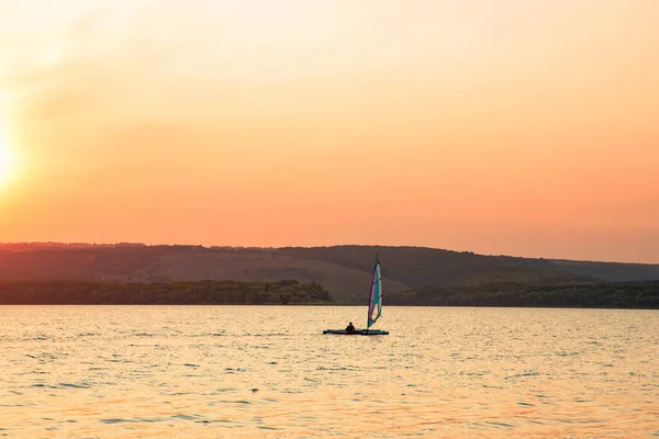 peaceful idyllic nature scenic view lake reservoir calm water environment and main land background in evening orange sun light with small sail boat of fisher man person