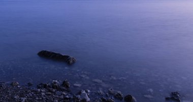 Yerel kıyı şeridinin uzun pozlama fotoğrafçılığı manzaralı bulanık su yüzeyi ve alacakaranlık ışıklı poster konsepti üzerinde taş ve metin için boş kopya alanı