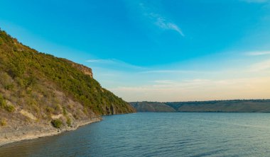 Yaz mevsiminde nehir sularının üzerindeki kayalık tepenin huzurlu sabah manzarası.