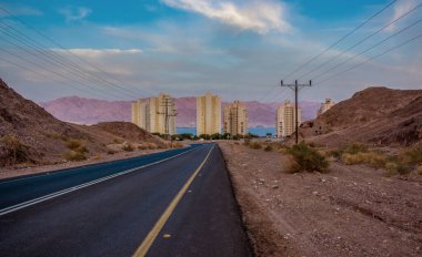 Şehrin kenar mahallelerinde kum taşı çevre alanı. Ortadoğu bölgesi binaları çöl tepeleri arasında arabasız asfalt yol manzaralı.