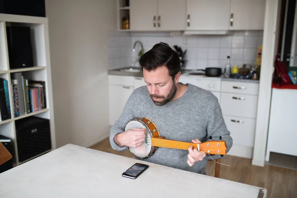Telleri cep telefonu uygulaması ile değiştirdikten sonra banjo ukulele ayarlayan adam