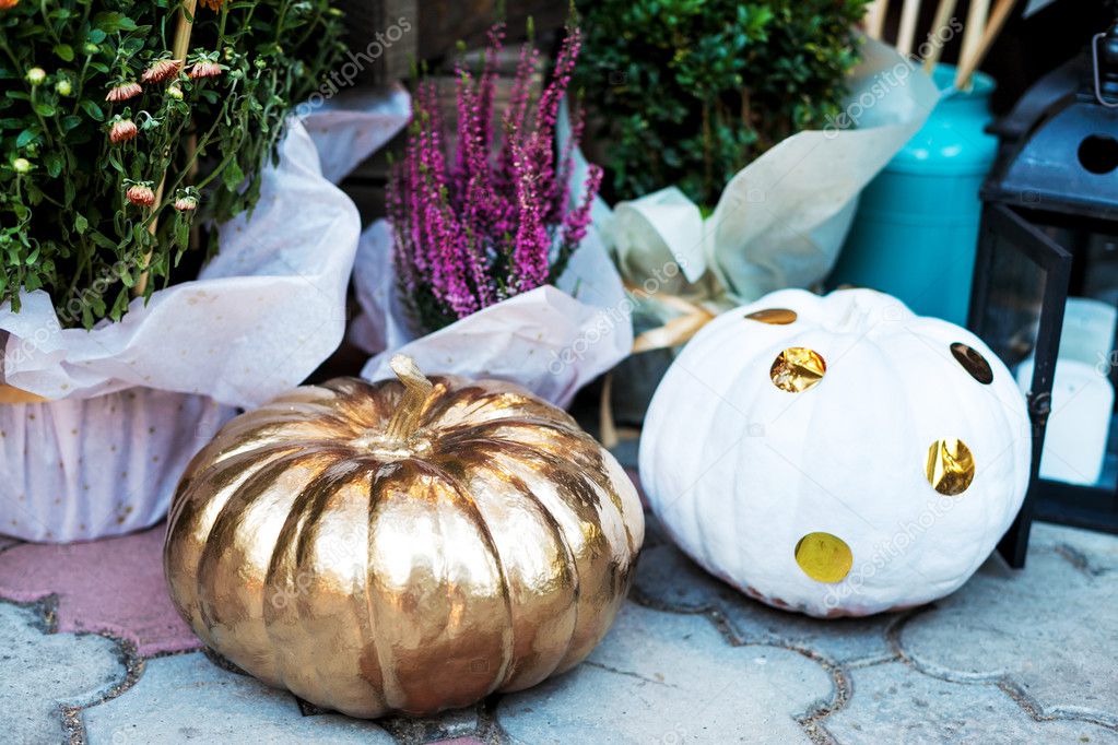 Halloween pumpkins painted in white and gold. Holiday decoration.Flowers and paper pin wheels
