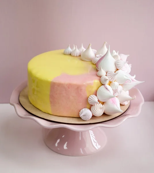Rosa mousse tårta täckt med gula och rosa choklad mirror glaze och maräng kyssar. Rosa porslin stativ. Rosa bakgrund. Naturligt ljus. — Stockfoto